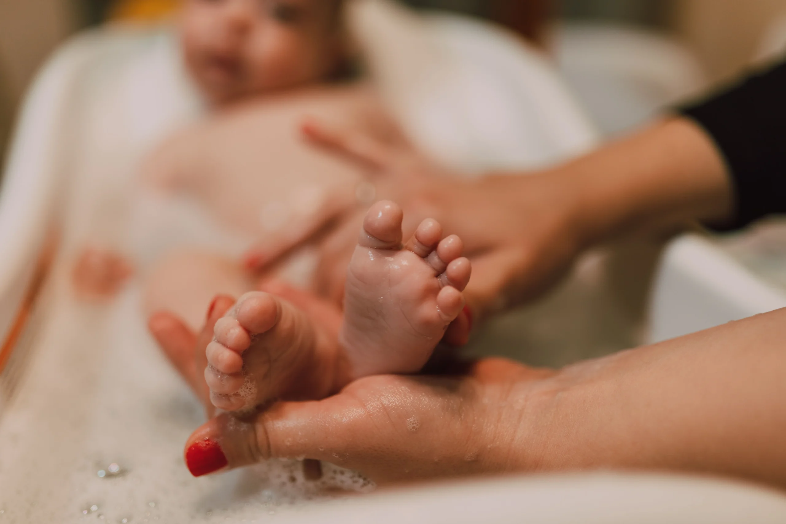 Mains d'un parent tenant délicatement les petits pieds mouillés d'un bébé dans la baignoire.
