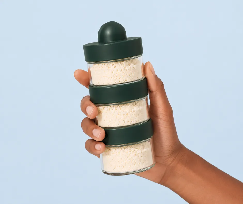 Main tenant le doseur de lait en verre BeDose pour comparer avec un doseur plastique Béaba.